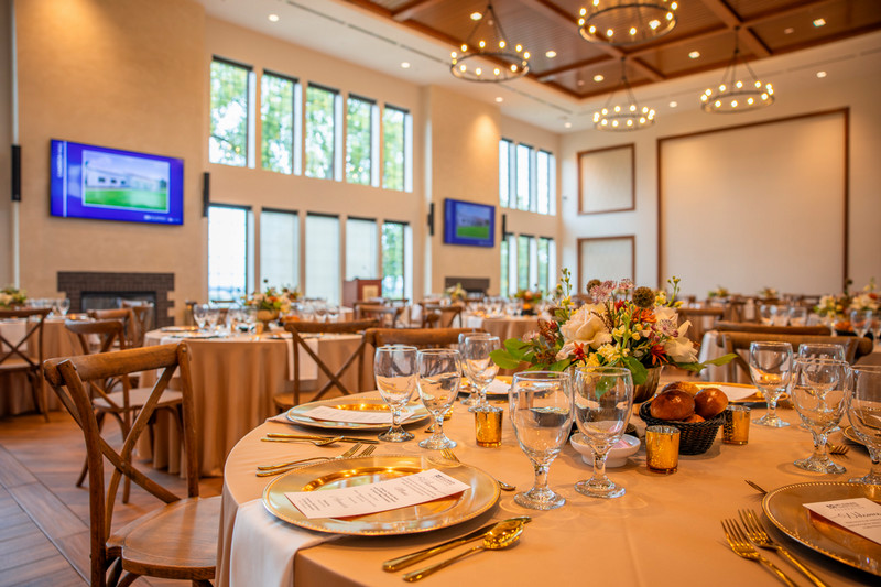 Elegant banquet setup in a spacious hall featuring beautifully arranged tables with floral centerpieces and golden accents.